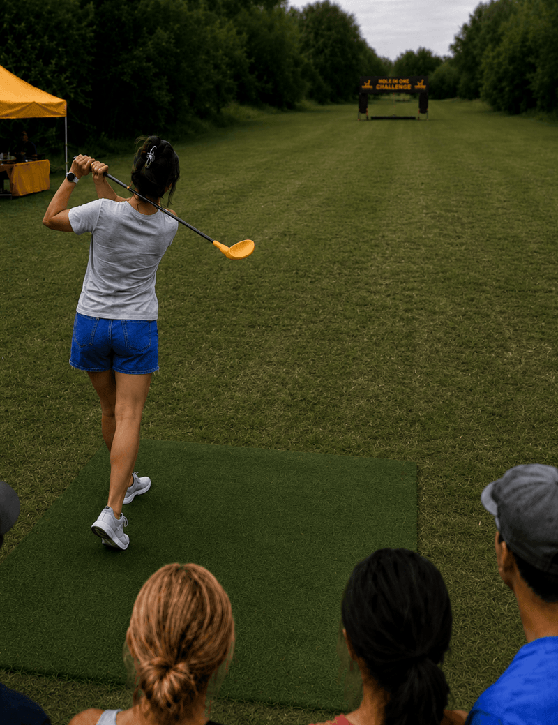 Person practicing golf swings on a driving range with onlookers watching. Bananas Golf - Raleigh, NC - Triangle Area - Nerf Golf Hole In One Nerf Golf Challenge 